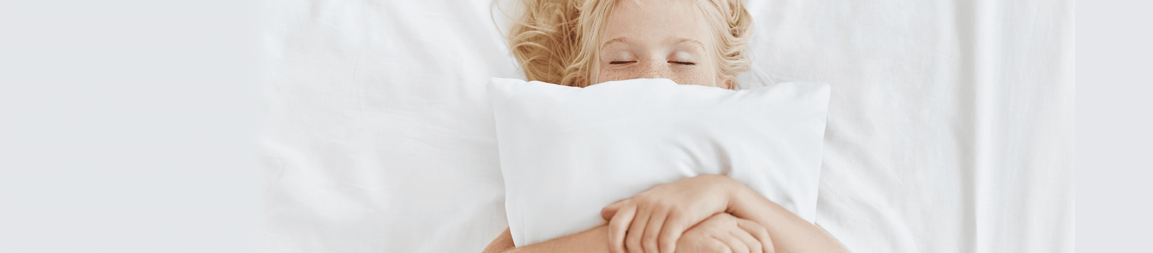 Carefree restful little girl lying on white bedclothes, embracing pillow while having pleasant dreams  Blonde girl with freckles sleeping in bed after spending all day at picnic  Restful child