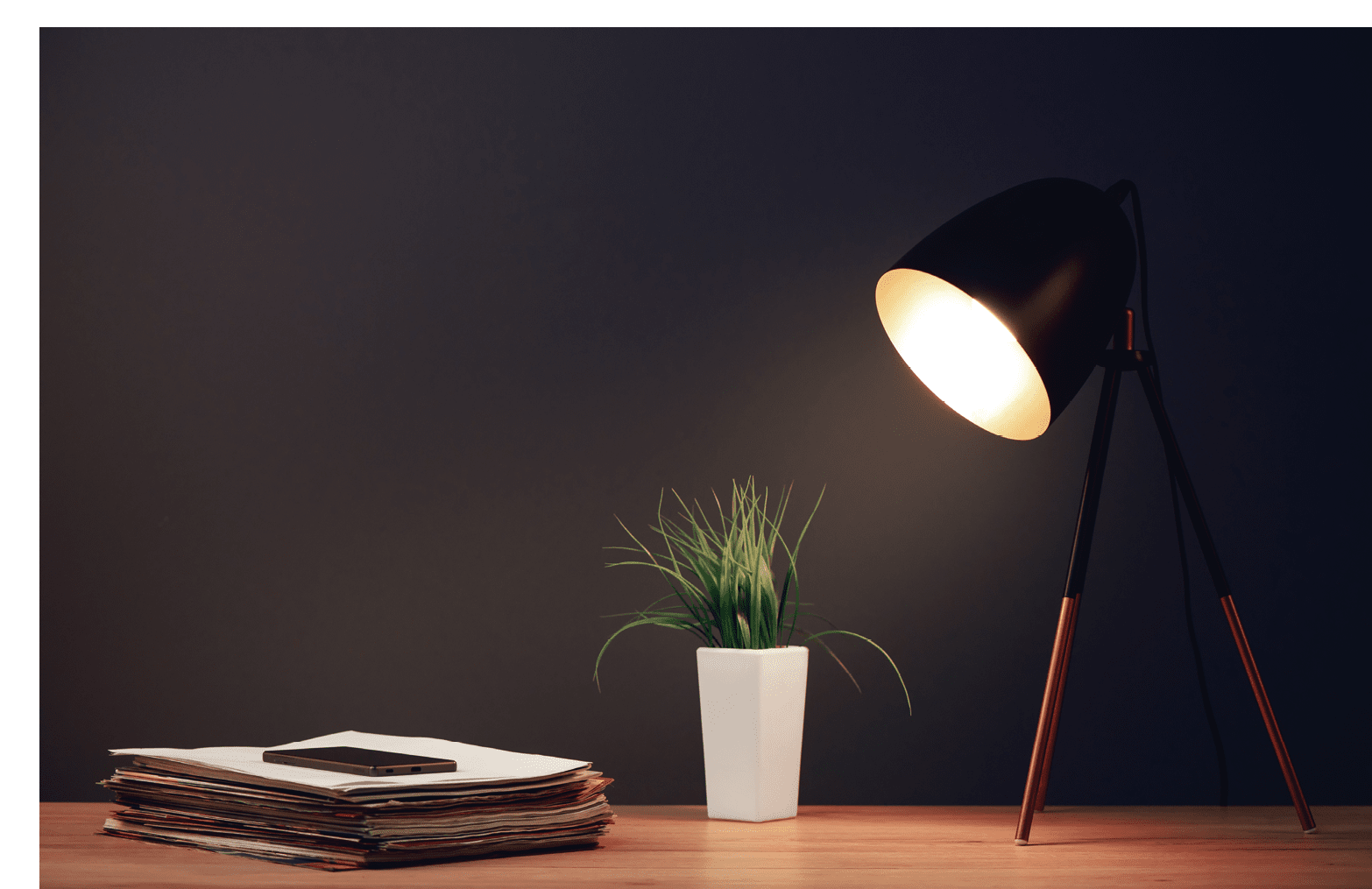 Office work desk with lamp, mobile phone, stack of newspapers and green plant in pot