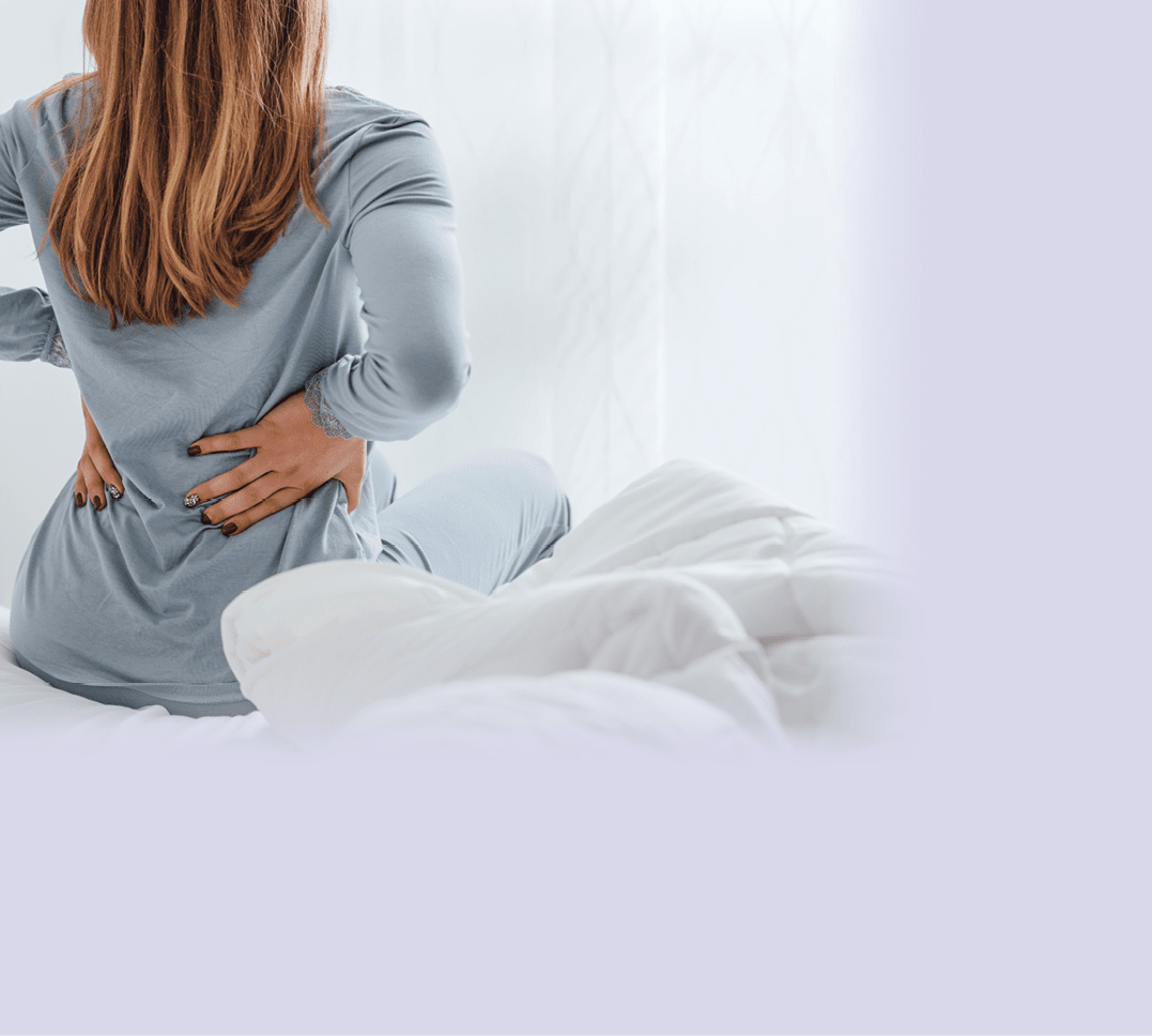 Young woman with back ache, she is sitting on the bed and touching her back
