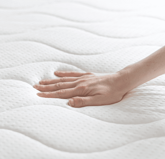 cropped shot of female hand testing new white orthopedic mattress on firmness in furniture store, memory foam surface, closeup