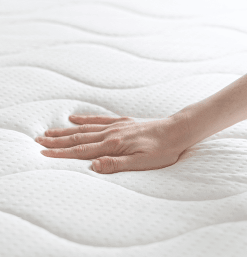cropped shot of female hand testing new white orthopedic mattress on firmness in furniture store, memory foam surface, closeup