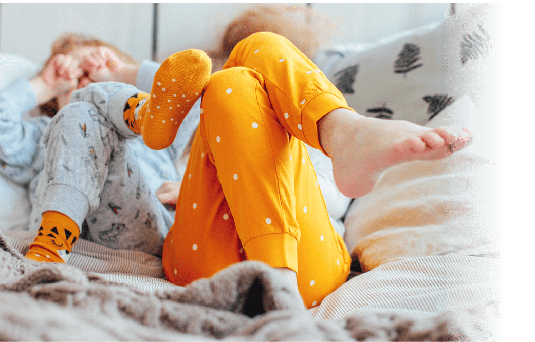 Little pretty brother and sister in pajamas lying in bed, cozy morning, focus on legs