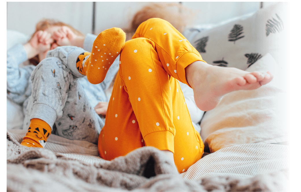 Little pretty brother and sister in pajamas lying in bed, cozy morning, focus on legs