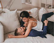 Young caucasian couple cuddling on couch at home on weekend. Beardy Italian man laying on sofa with wife on vacation. Tanned hispanic girl embracing boyfriend. Honey moon. Newlyweds, romance, lovers