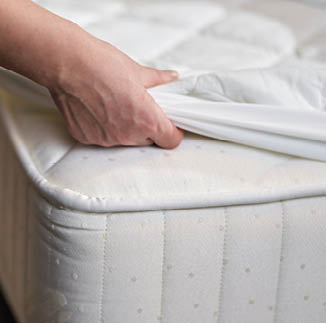 Close up of maid changing clean sheet on white mattress in hotel room while cleaning. Hotel service concept