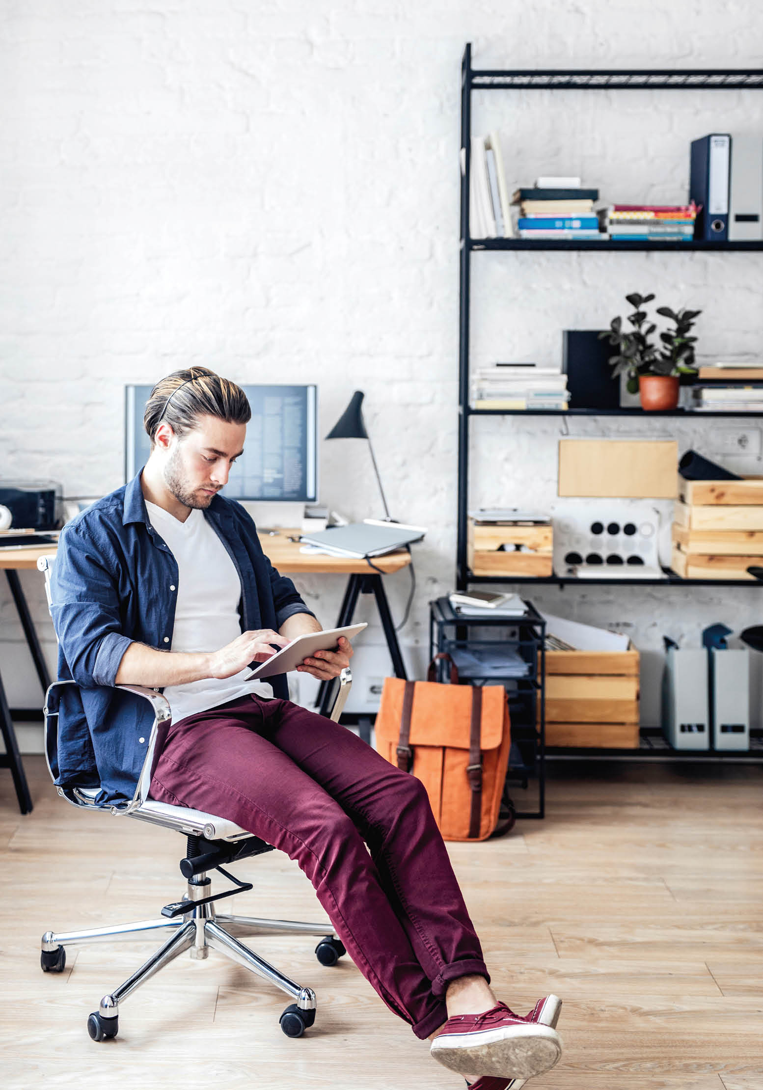 Handsome young Caucasian businessman sitting at modern home office and reading on tablet.