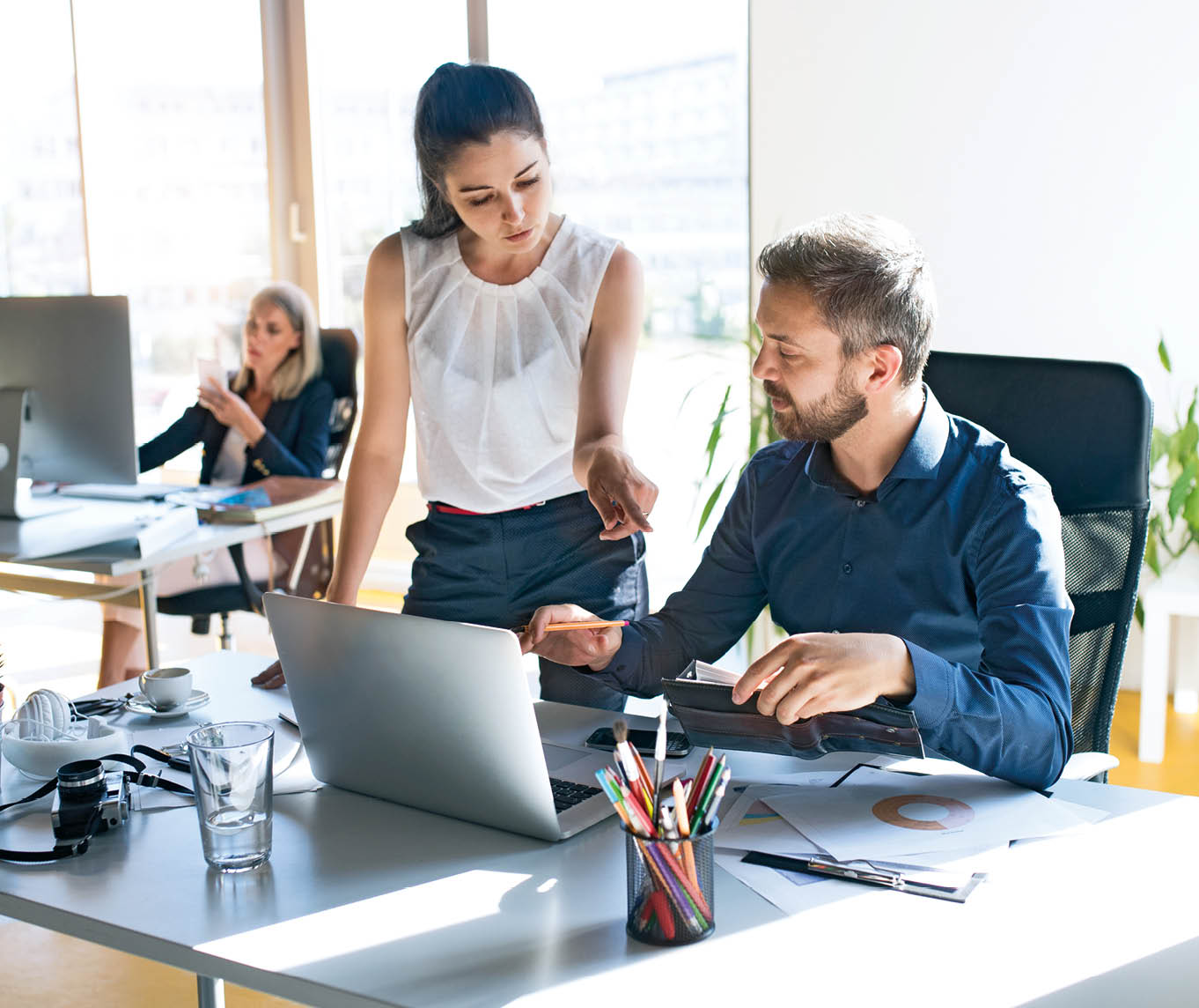 Three business people in the workplace. Two women and man sitting in the office working together.