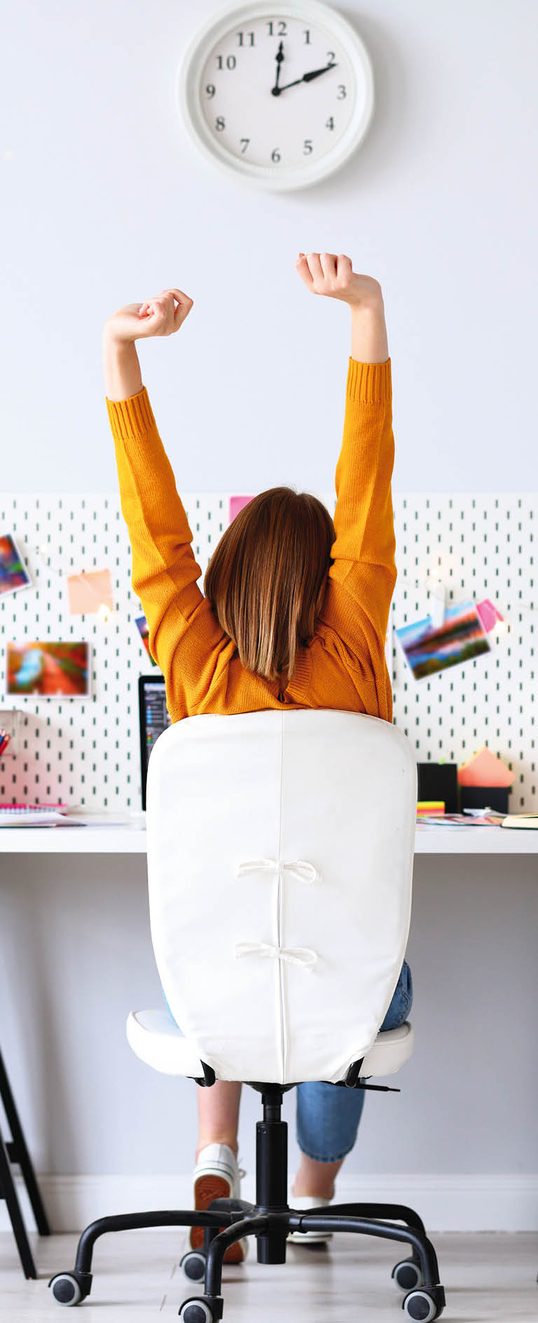 Back view of anonymous woman stretching arms during break in work while sitting at desk in home office 