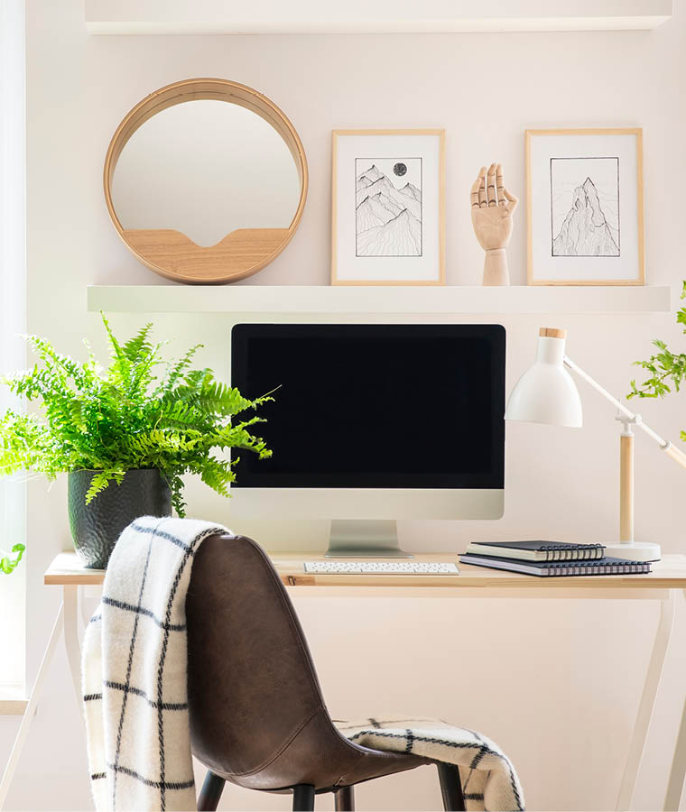 Shelves with illustrations above a wooden desk with computer by a window in a natural, white home office interior for an artist