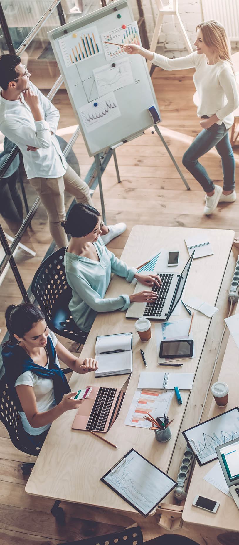 Top view of multiracial young creative people in modern office. Group of young business people are working together with laptop, tablet, smart phone, notebook. Successful hipster team in coworking. Freelancers.