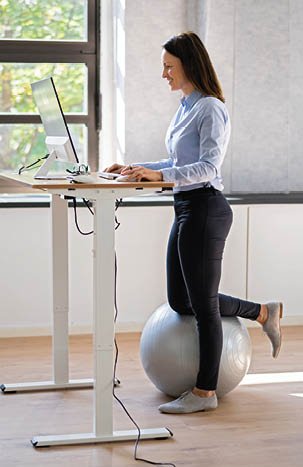 Woman Using Adjustable Height Standing Desk In Office For Good Posture