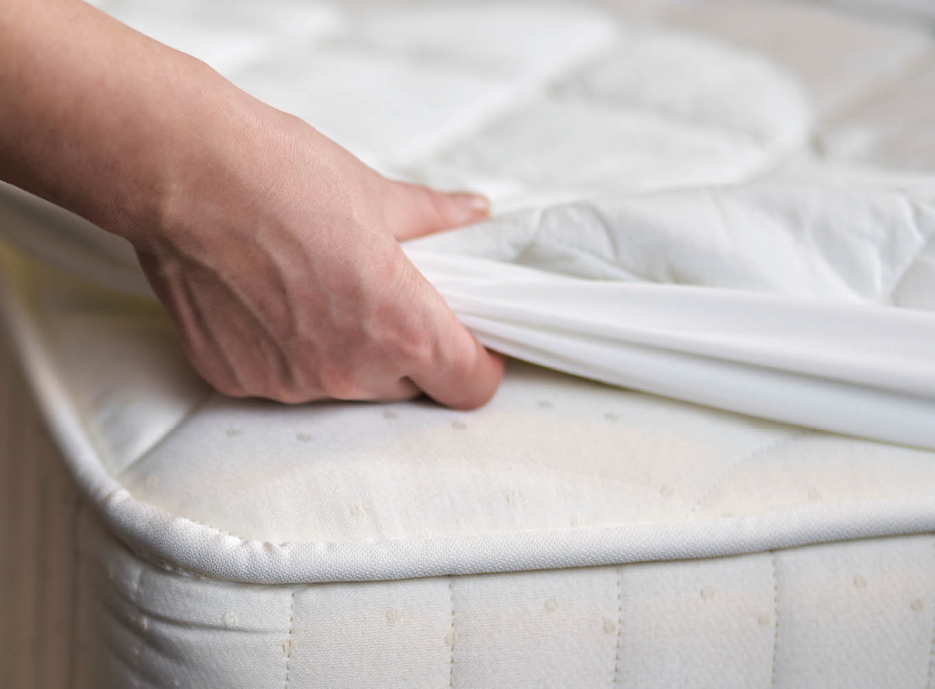 Close up of maid changing clean sheet on white mattress in hotel room while cleaning. Hotel service concept