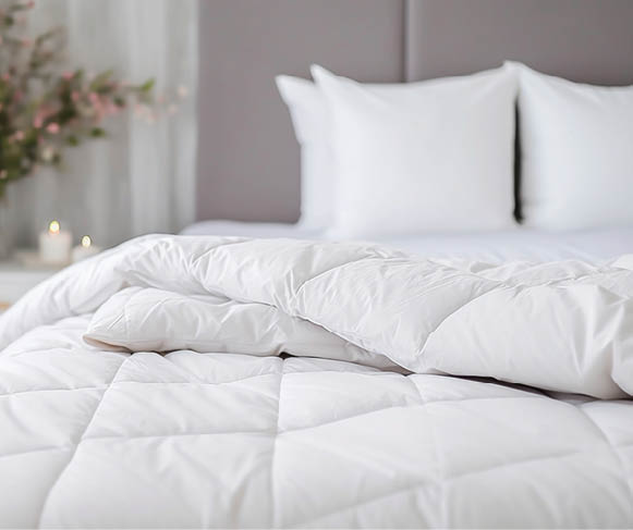 white soft duvet lying against background headboard with pillows,bedside table with flowers,candles,close-up,concept preparing for winter season,household chores,comfort in house,hotel,home textiles