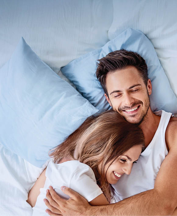 Top view of beautiful happy young couple lying on bed and hugging