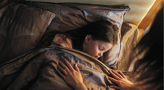 Sleeping child mother care. Night rest. Woman covering peaceful calm daughter with blanket lying in bed at late night in dark home bedroom.