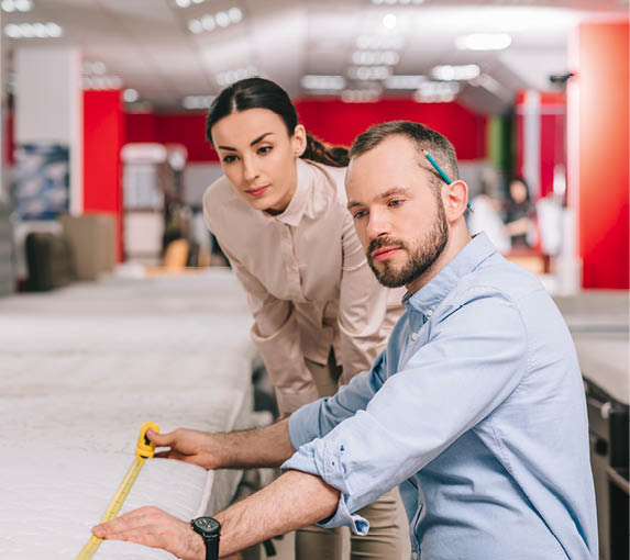 couple measuring mattress with measure tape in furniture store with arranged mattresses