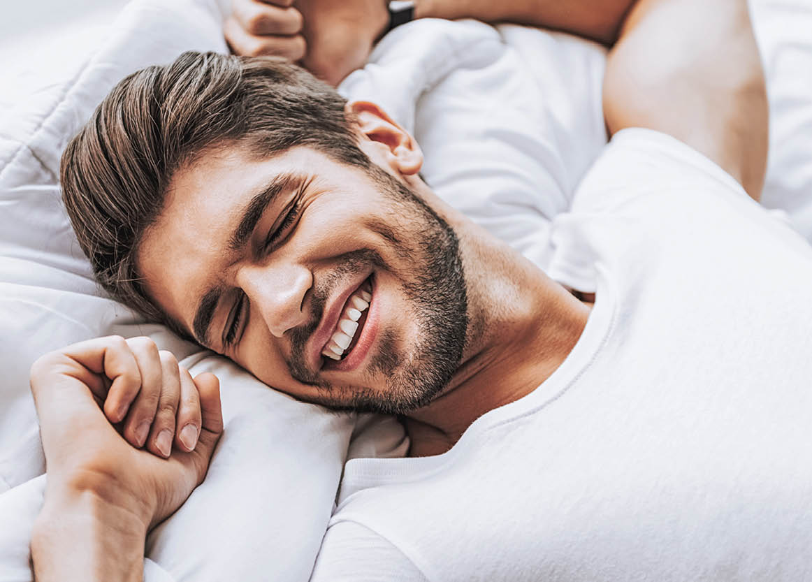 It is going wonderful day. Close up top view portrait of happy relaxing man waking up and enjoying stretching in bed