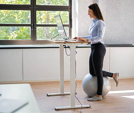 Woman Using Adjustable Height Standing Desk In Office For Good Posture