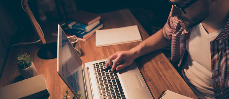Top view portrait of attractive, busy, smart man in shirt with stubble having notepad with pencil, holding arm on keypad, working at night time, sitting in workplace, workstation