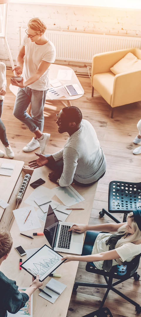 Top view of multiracial young creative people in modern office. Group of young business people are working together with laptop, tablet, smart phone, notebook. Successful hipster team in coworking. Freelancers.