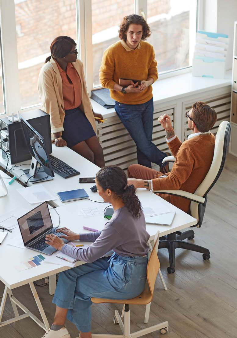 Vertical high angle view at multi-ethnic IT development team collaborating on business project while working in software production studio