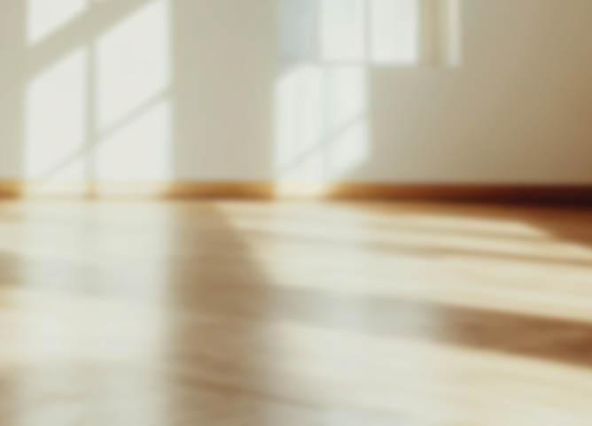 Empty modern room with sunlight streaming through a large window, creating warm shadows on white walls and polished wood floors.