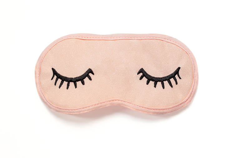 Pastel pink sleep mask with closed eyes embroidered on it with eyelashes on white background. Top view, flat lay. Concept of vivid dreams. Accessories for girls and young women