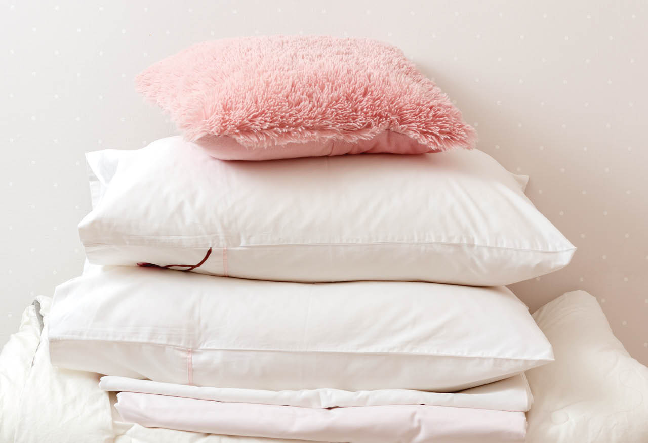 A pile of clean ironed bedding and a towel lies on the dresser.