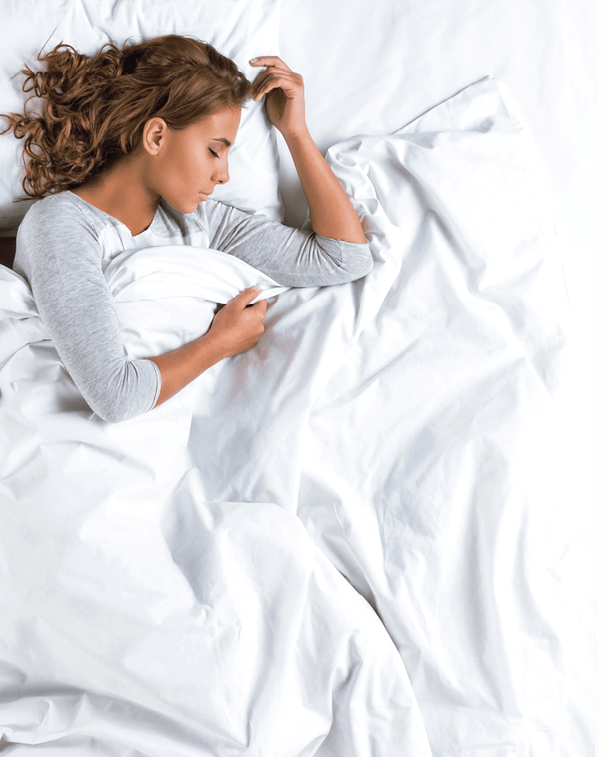 Top view photo of beautiful mixed-race girl sleeping on big white bed. Young pretty woman wearing pajamas. Girl lying on side under blanket