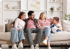A family of four, including two adults and two children, are sitting on a couch together. AI generated content