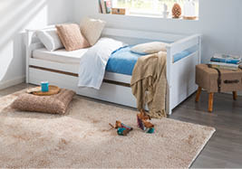 A bedroom with a white bed and a blue blanket. A teddy bear is on the floor. A book is on the nightstand. AI generated content