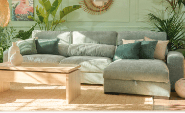 A large, light grey couch is placed in a living room with a window behind it. The couch is positioned in front of a potted plant and a vase. AI generated content
