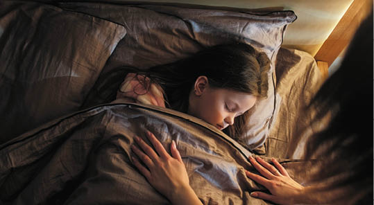 Sleeping child mother care. Night rest. Woman covering peaceful calm daughter with blanket lying in bed at late night in dark home bedroom.
