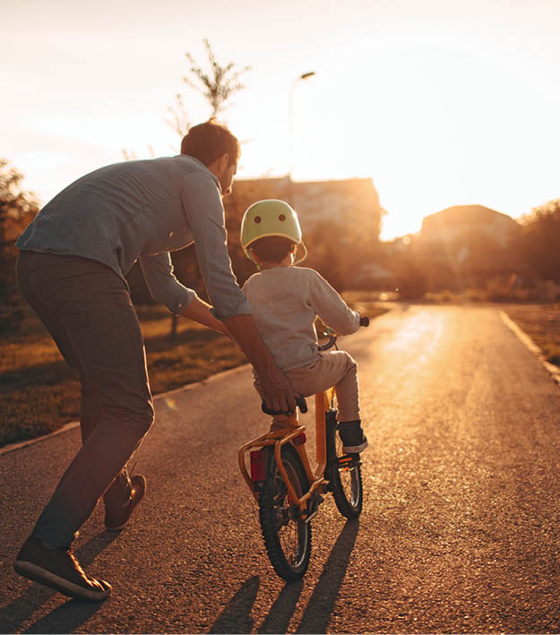 Photo of a young boy and his father on a bicycle lane, learning to ride a bike.
