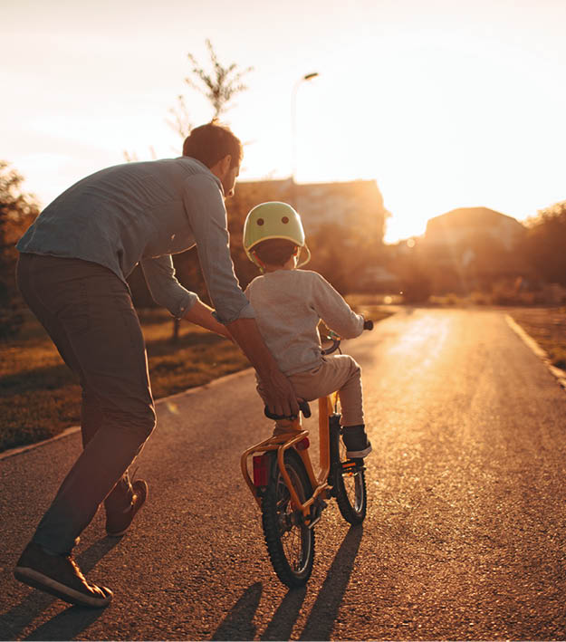 Photo of a young boy and his father on a bicycle lane, learning to ride a bike.