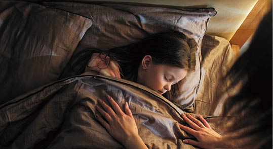 Sleeping child mother care. Night rest. Woman covering peaceful calm daughter with blanket lying in bed at late night in dark home bedroom.