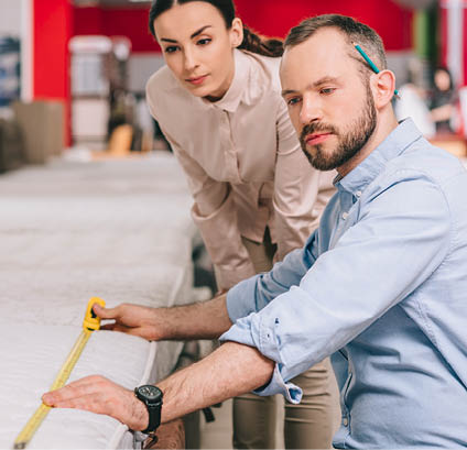 couple measuring mattress with measure tape in furniture store with arranged mattresses