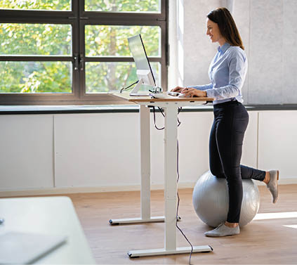 Woman Using Adjustable Height Standing Desk In Office For Good Posture
