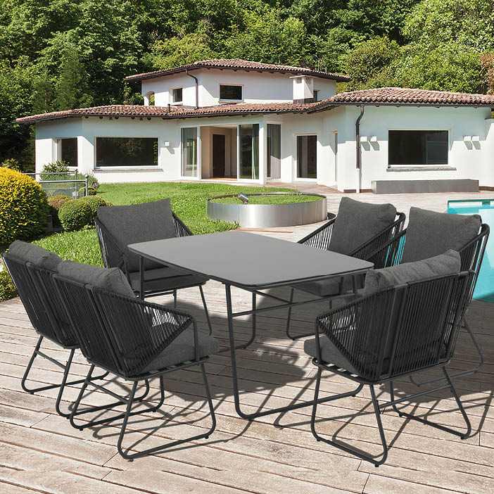 A patio set with a glass table and four chairs, two on each side. The chairs are black and the table is gray. The patio is located in front of a house. AI generated content