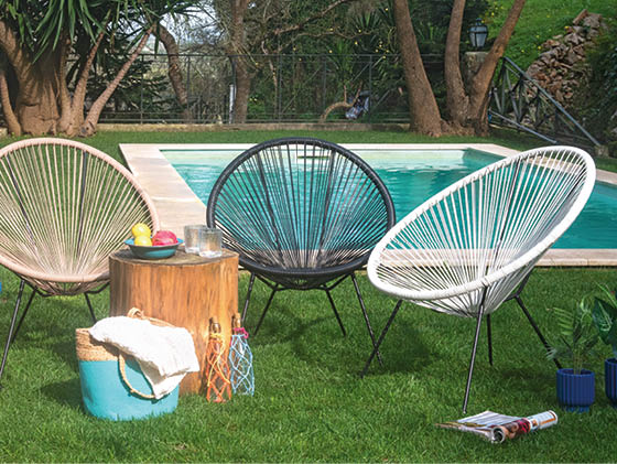 A group of four chairs are arranged on a grassy area, with a pool in the background. There are also a few potted plants and a towel nearby. AI generated content
