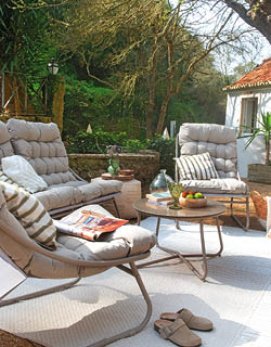 A patio set with a couch, chair, and table. The couch is covered with a striped blanket and a book. The chair is positioned next to the couch. There are two potted plants, one on the left and one on the right. A bowl is placed on the table. AI generated content