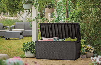 A black wicker trunk is sitting on a patio with a garden setting. AI generated content