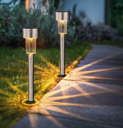 Two silver lights on a sidewalk, illuminating the grass. AI generated content