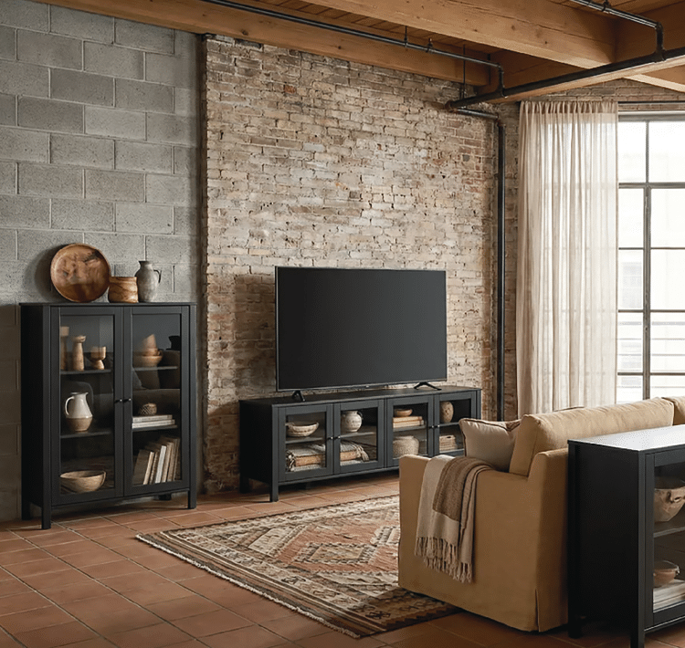 A large black flat screen TV is placed on a stand in a living room. The room is furnished with a couch, a chair, and a dining table. There are also several books scattered throughout the room, and a vase can be seen on a surface. The room has a brick wall and a window, providing natural light. AI generated content