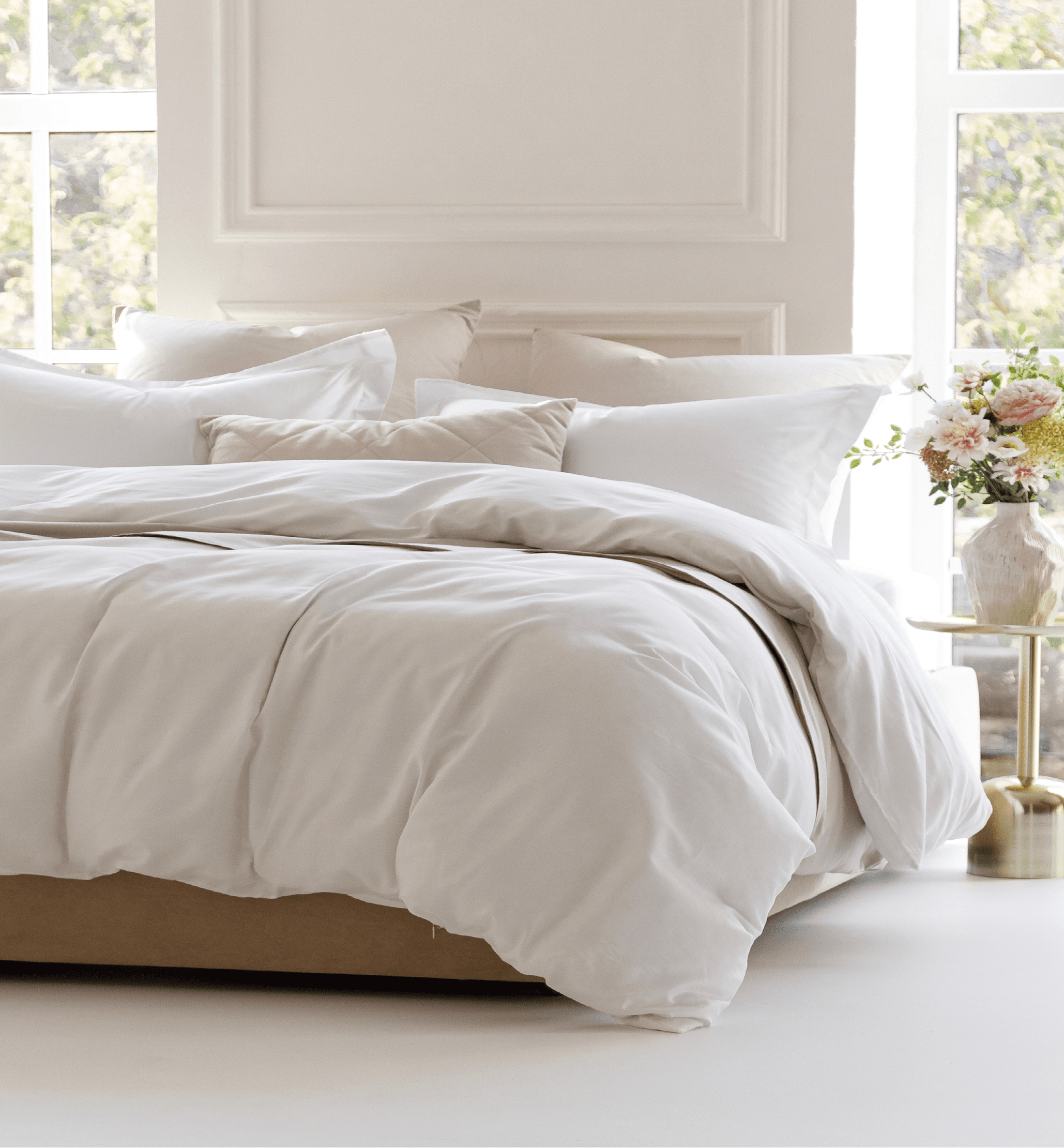 Sunny bedroom with two large windows. Four pillows, cushion and a fluffy down comforter on a double bed with bedside table and bouquet in vase on it. Side view horizontal photo. Suitable for mockup